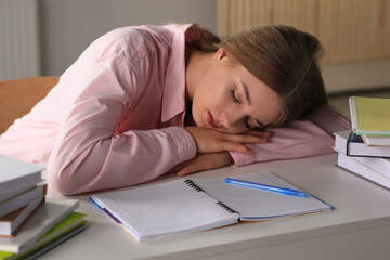 Young tired woman sleeping near books at white table indoors