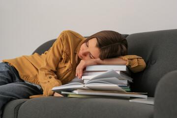 Fototapeta premium Young tired woman sleeping near books on couch indoors