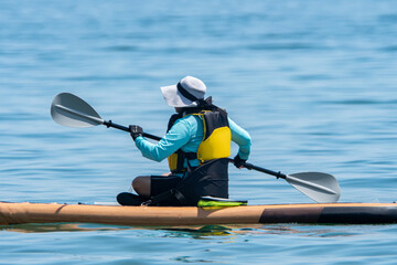 Woman sail on a SUP boards with special seating chair and wet suit and life jacket for paddling....