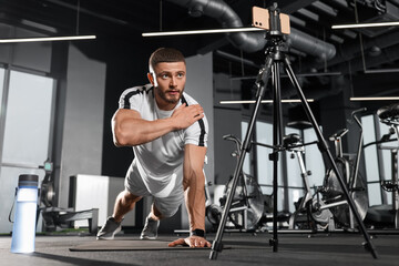 Trainer streaming online workout with phone at gym
