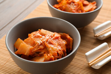 Bowls of spicy cabbage kimchi and chopsticks on bamboo mat, closeup