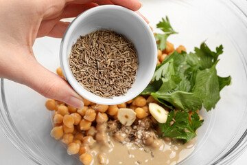Woman adding cumin into bowl with ingredients for delicious hummus, closeup
