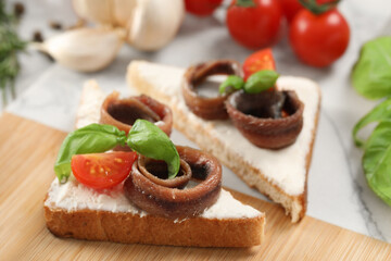 Delicious sandwiches with cream cheese, anchovies and tomatoes on wooden board, closeup