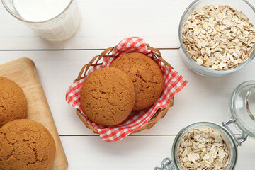 Delicious oatmeal cookies, flakes and milk on white wooden table, flat lay