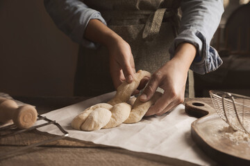 Woman making braided bread at wooden table, closeup. Traditional Shabbat challah