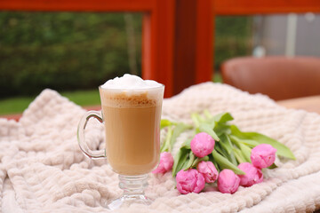 Glass of delicious cocoa and pink tulips on light blanket at terrace