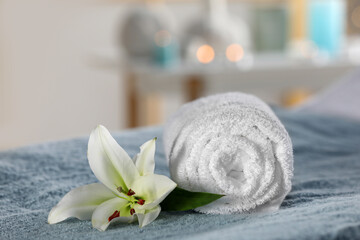 Spa composition with rolled towel and lily flower on massage table in wellness center