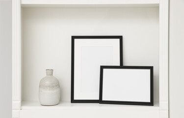 Fototapeta na wymiar Blank frames and ceramic vase on shelving unit indoors