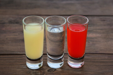 Shots with lime juice, tequila and sangria as colors of mexican flag on wooden table, closeup. Traditional serving