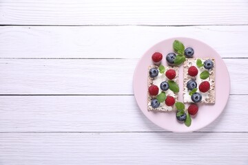 Fototapeta na wymiar Plate with crispbreads, berries and mint on white wooden table, top view. Space for text