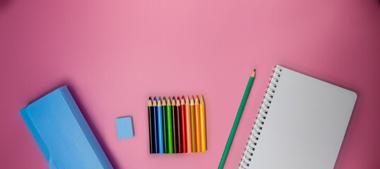 School supplies, colored pencils, eraser, pencil, penal and notebook on a pink background. School concept. School education materials, copy space, top view.