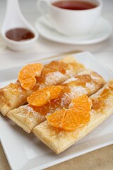 Fresh tasty puff pastry with sugar powder and tangerines on table, closeup