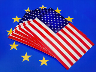 Stacks of US flags are lying on top of an EU flag