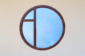 Round window with sky reflection in mirror on yellow cement wall background.