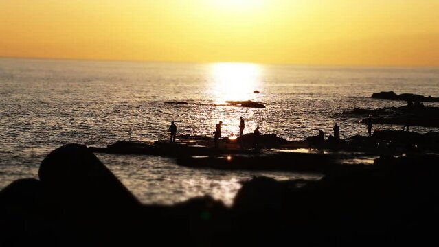 江ノ島の磯で釣りをする人々の夕陽によるシルエット