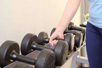 Fototapeta na wymiar Woman in the gym takes a dumbbell from the rack. Black metal dumbbells of different weights on a rack in a gym. Sports equipment for increasing muscle mass. The concept of doing sports.