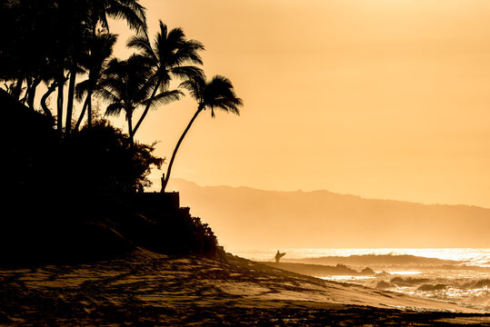 Silhouette of a surfer with a surfboard in the distance at sunset on Sunset Beach, Hawaii 