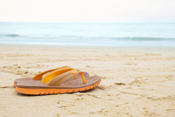 Flat beach flip flops on the background of yellow sand and sea waves. Beach holiday concept. Banner...