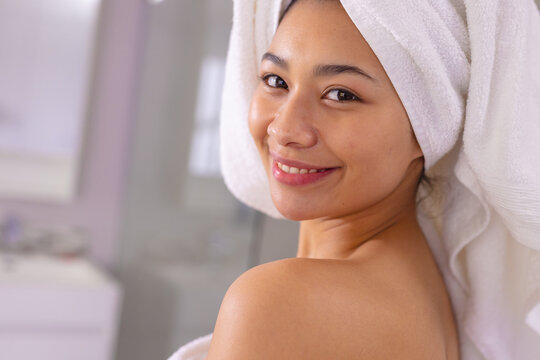 Portrait of happy biracial woman wearing towel smiling in bathroom, with copy space