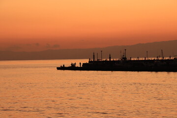 Fototapeta premium 漁港にある防波堤で釣りをする人のシルエットの夕景