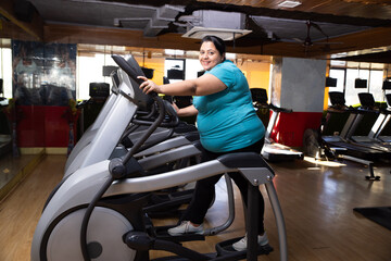 Young overweight indian woman is workout in gym to lose weight. Asian female doing cardio training on bicycle machine. Full length.