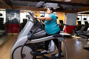 Young overweight indian woman is workout in gym to lose weight. Asian female doing cardio training...