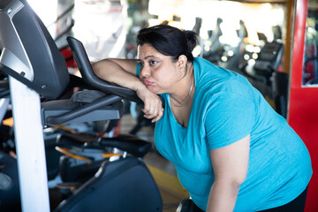 Fototapeta na wymiar Tired overweight indian woman sitting on treadmill in gym. Closeup.