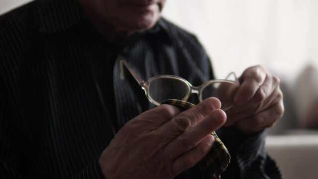 a pensioner wipes old glasses from dirt and dust with a napkin. an elderly man cleans the lenses of glasses. loss of vision in old age. selective focus
