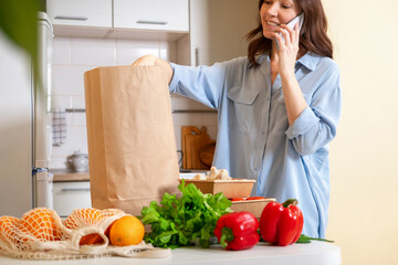 Young woman checking her fresh groceries delivery ordered from internet. Fresh organic vegetables, greens and fruits. Kitchen interior. Food delivery concept