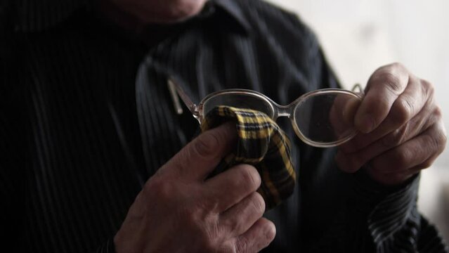 hands of an elderly man wipes his glasses from dirt and dust with a napkin. a pensioner cleans the lenses of his glasses. loss of vision  selective focus. lifestyle of an old man. eye fatigue
