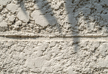 white exterior cement wall rough surface The morning sun and the shadow of the leaves Uneven texture and background with shadows of plants.