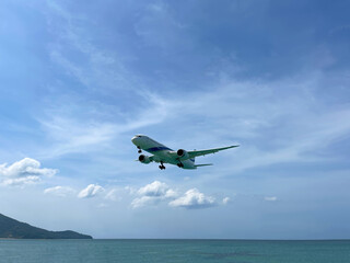 Fototapeta na wymiar Plane takes off over the sea. Beautiful photo. Blue sky with clouds. Land and green hills on the horizon. Passenger, cargo transportation. Boeing 787-8 aircraft model. Aviation. Airplane in flight.