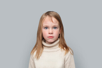 Portrait of serious funny little girl looking at camera on grey background