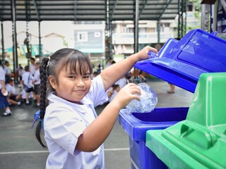 Elementary school students are throwing garbage into the bin with a smiling face.