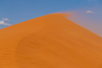 Fototapeta na wymiar Telephoto shot of Dune 45, Namibia, with distant climbers on top, in a sand storm.