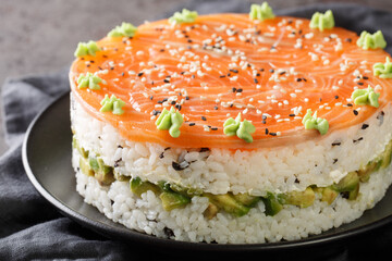 Delicious philadelphia sushi cake with red fish, rice, avocado, cream cheese, seaweed, sesame seeds decorated with wasabi close-up in a plate on the table. Horizontal