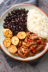 Venezuelan Shredded Beef Pabellon Criollo with rice, black beans and fried plantains closeup on the plate on the table. Vertical top view from above
