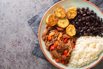 Pabellon criollo is a traditional dish of Venezuela with black beans, rice, plantains and shredded steak that have been cooked with tomatoes closeup on the plate. Horizontal top view from above