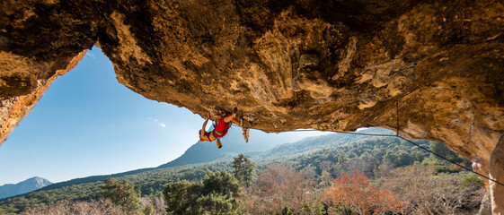 A young rock climber on an overhanging cliff. The climber climbs the rock. The girl is engaged in...