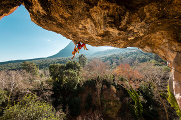 girl rock climber climbs a rock against the backdrop of a forest and blue mountains. rock climber...
