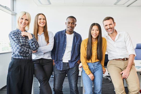 Group shot of diverse casual business people standing in office smiling at camera