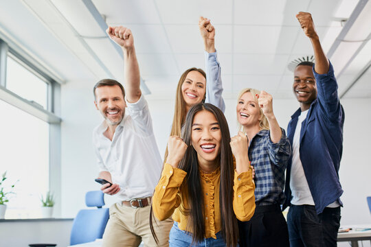 Portrait of diverse group of colleagues cheering together in office