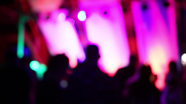 Blurred silhouettes of crowd of people dancing on the dance floor of a night club under the light of colored spotlights and lasers.