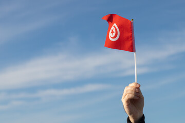 Tunisian flag in hand flutters in the wind against the sky