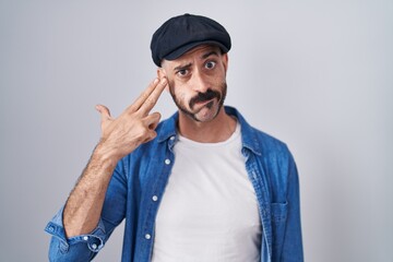 Hispanic man with beard standing over isolated background shooting and killing oneself pointing hand and fingers to head like gun, suicide gesture.