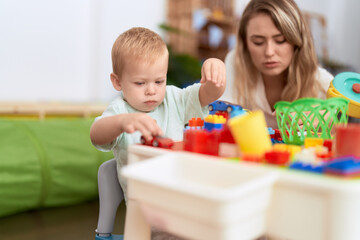 Obraz na płótnie Canvas Teacher and toddler playing with construction blocks and car toy sitting on table at kindergarten