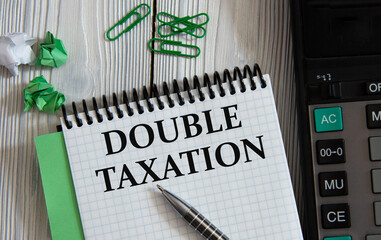 DOUBLE TAXATION - words on a white notepad on the background of a calculator, paper clips