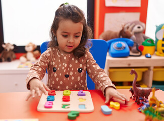 Adorable hispanic girl playing with maths puzzle game sitting on table at kindergarten