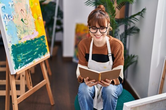 Young woman artist smiling confident reading book at art studio