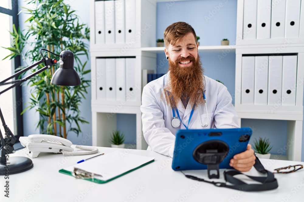 Wall mural young redhead man wearing doctor uniform using touchpad at clinic